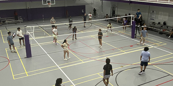Overhead view of students playing volleyball on indoor courts inside a recreation facility.
